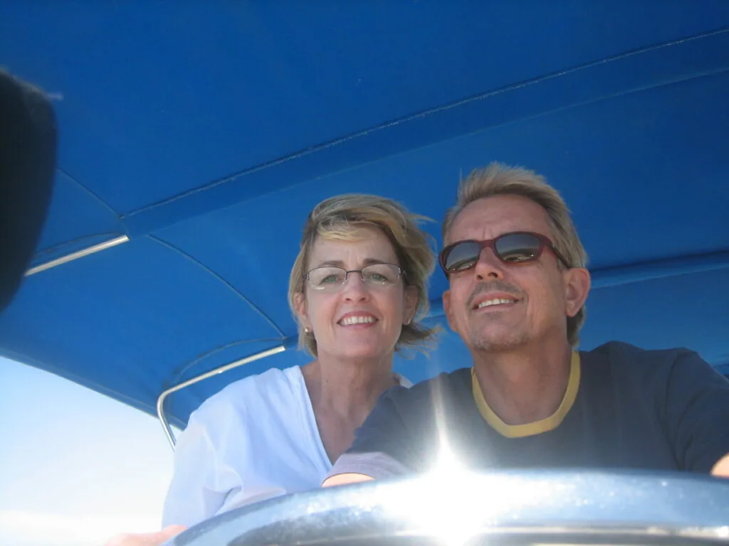 Two people smiling at camera under blue awning or cover with bright sunlight