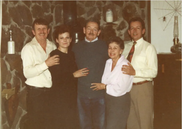 Five people posing together indoors in front of a patterned wall with mid-century decor