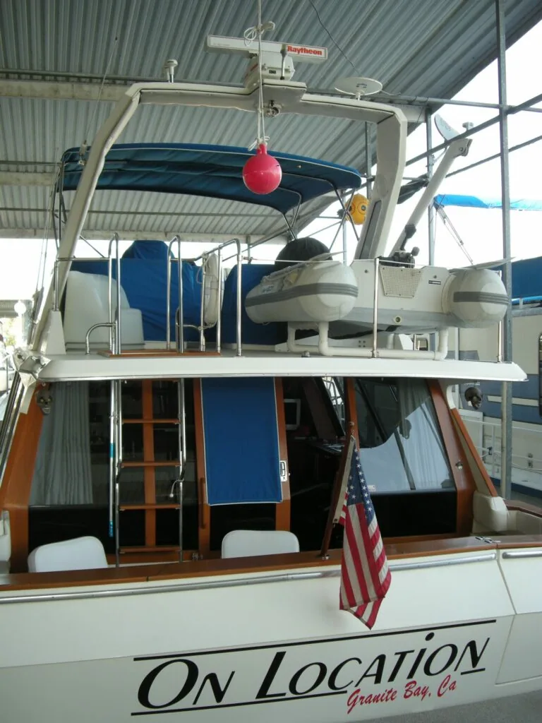 Rear view of white boat with blue awning, red buoy, and American flag docked under metal roof