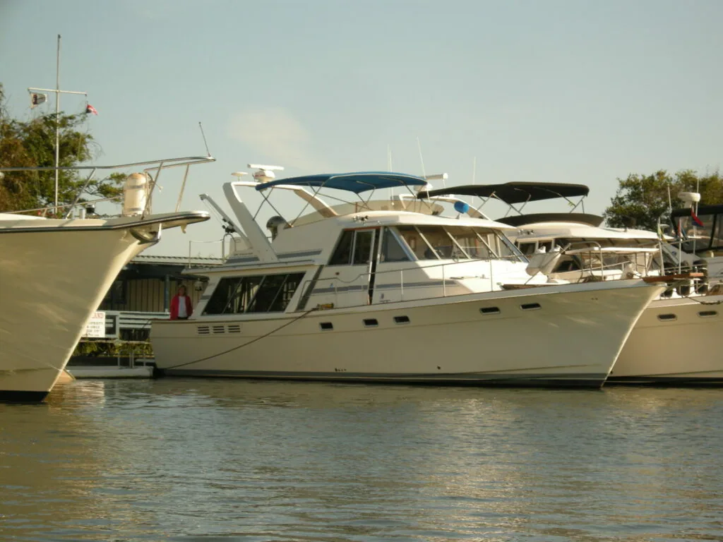 White motor yacht with blue awnings moored at dock alongside other boats