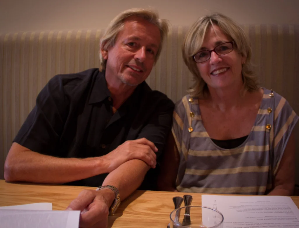 Two people smiling at a table with papers and a glass of water in front of them