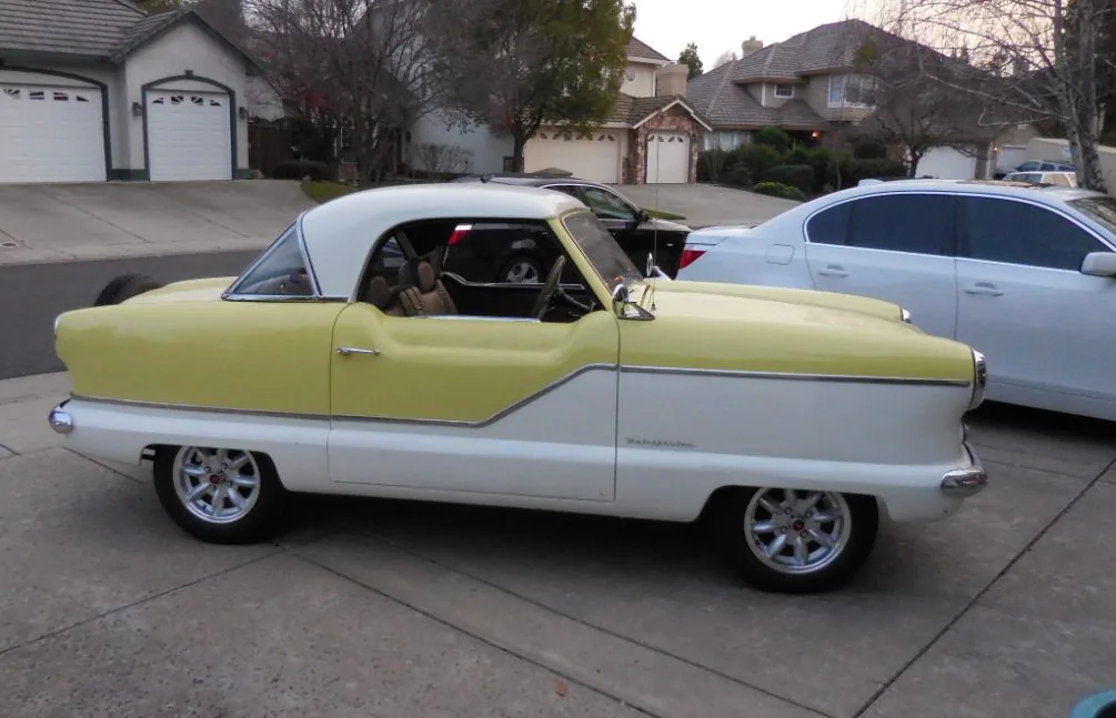 Yellow and white convertible classic car parked in residential driveway with houses in background