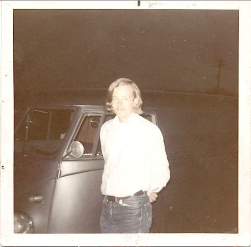Man in white shirt and jeans standing beside vintage car