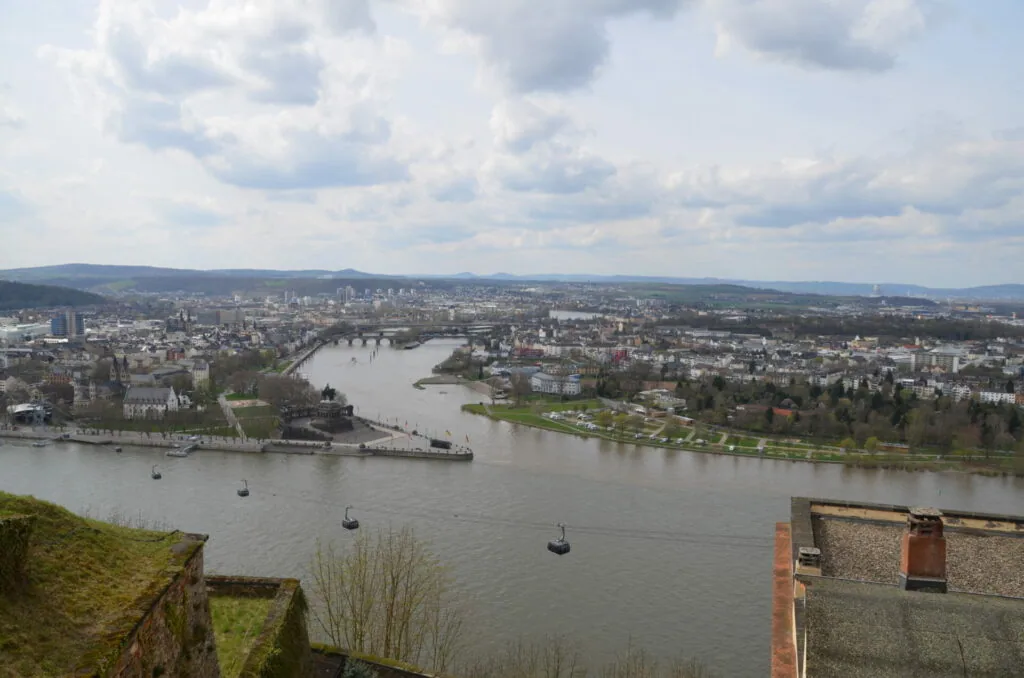 Aerial view of a European river valley city with bridges, buildings, and green landscapes under cloudy sky