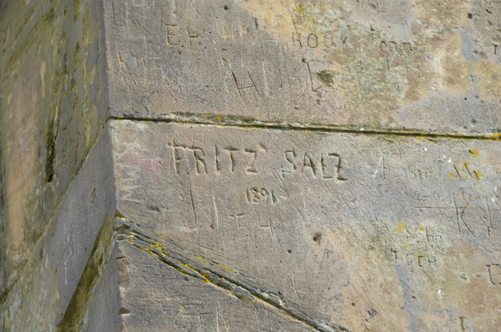 Carved stone surface with engraved text reading 'FRITZ SAIZ' and the date '1891', with moss growth and weathering visible