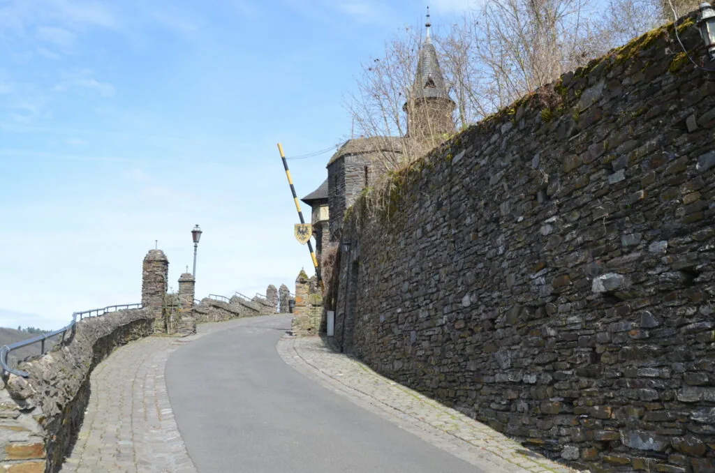 Curved stone pathway along ancient castle walls with tower visible in background under clear sky