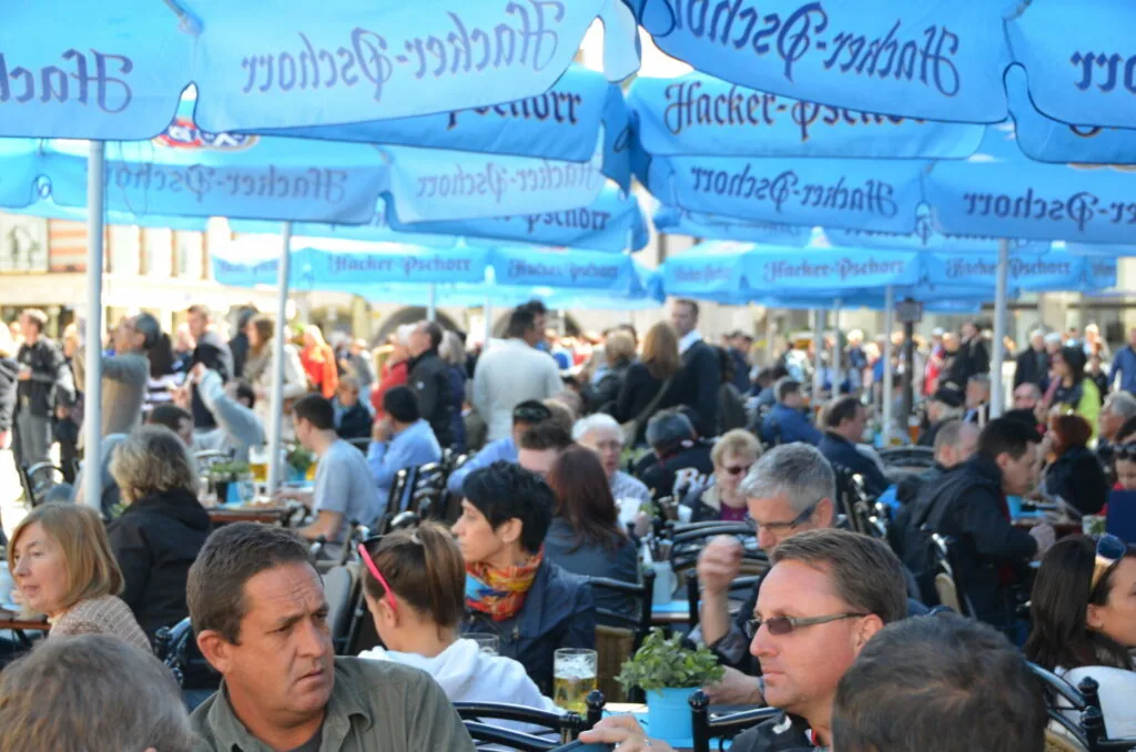 Crowded outdoor festival or market under blue tents with many people seated at tables