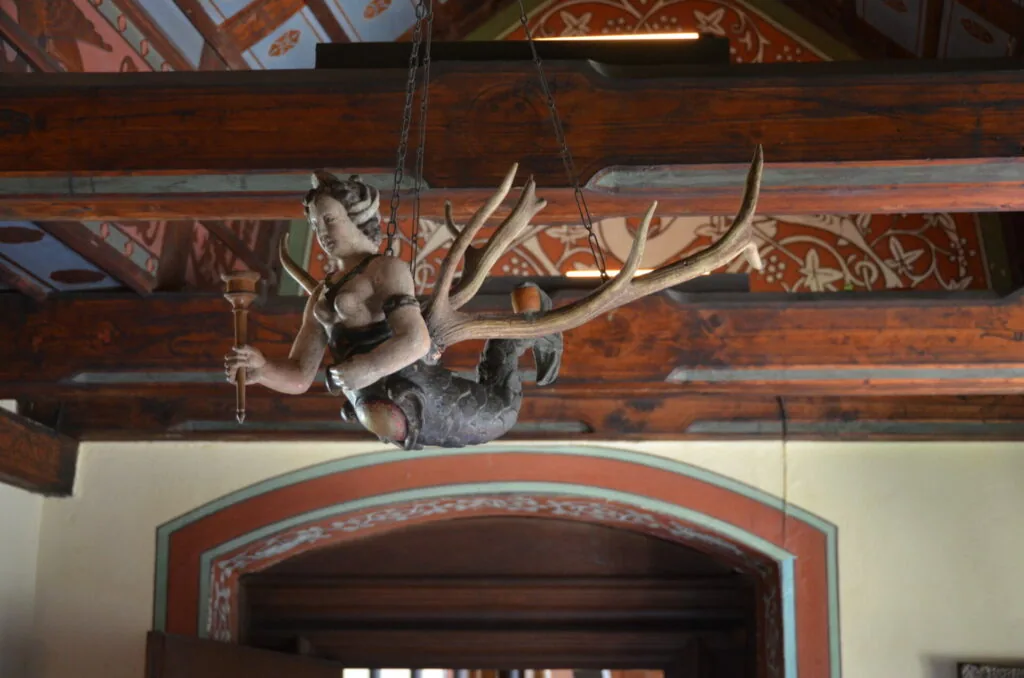 Ornate metal deer head sculpture with large antlers suspended from wooden beam above arched doorway in traditional interior