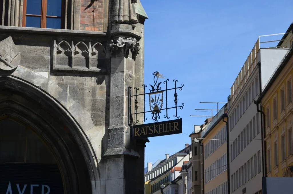 Historic European street with ornate wrought iron Ratskeller sign hanging from stone building with Gothic architectural details