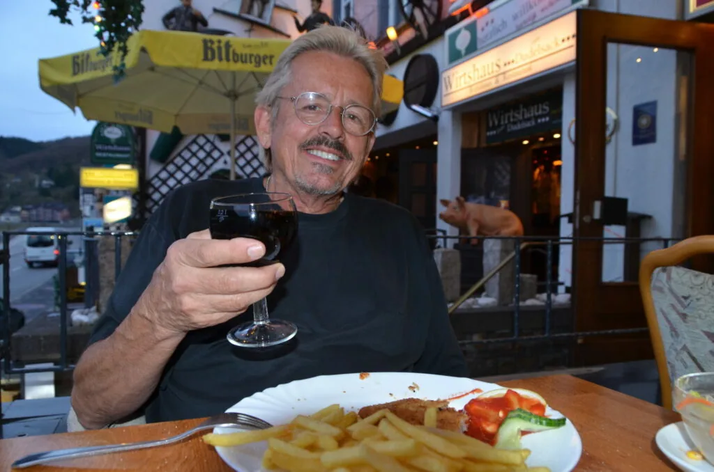 Man holding wine glass at outdoor café table with meal and yellow Bitburger umbrella visible