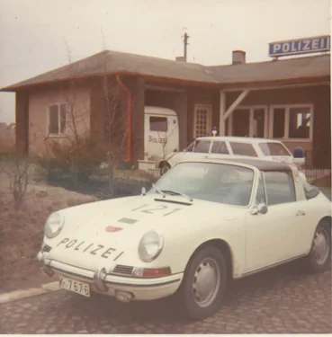 White Porsche police car parked in front of red brick police station building with Polizei sign