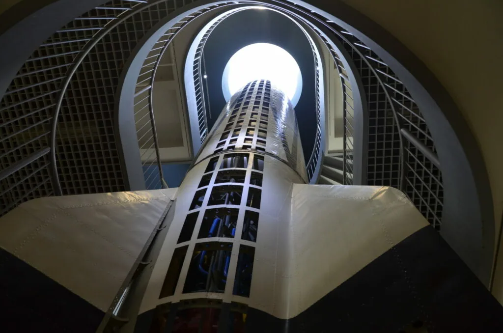Upward view of a cylindrical modern building with grid-patterned facades converging toward sky and circular opening at center