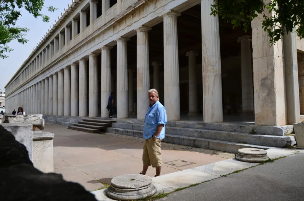 Man in blue shirt standing before ancient Greek temple with tall Doric columns