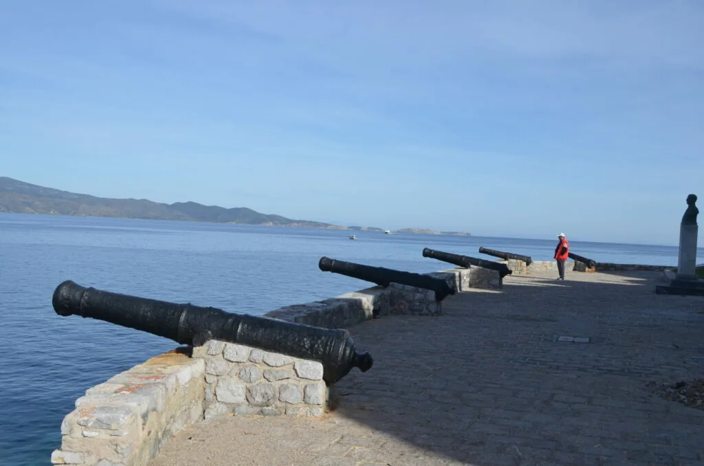 Historic cannons mounted on stone fortification overlooking Mediterranean sea with mountains in distance