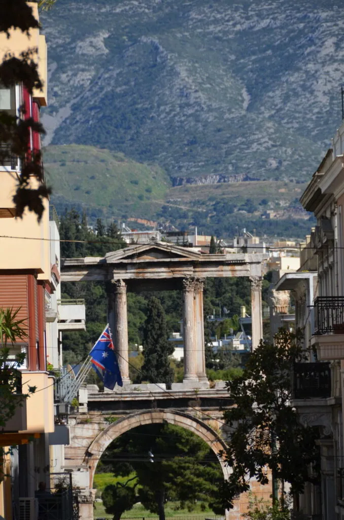 Ancient Greek temple with Corinthian columns framed between European buildings with mountains in background