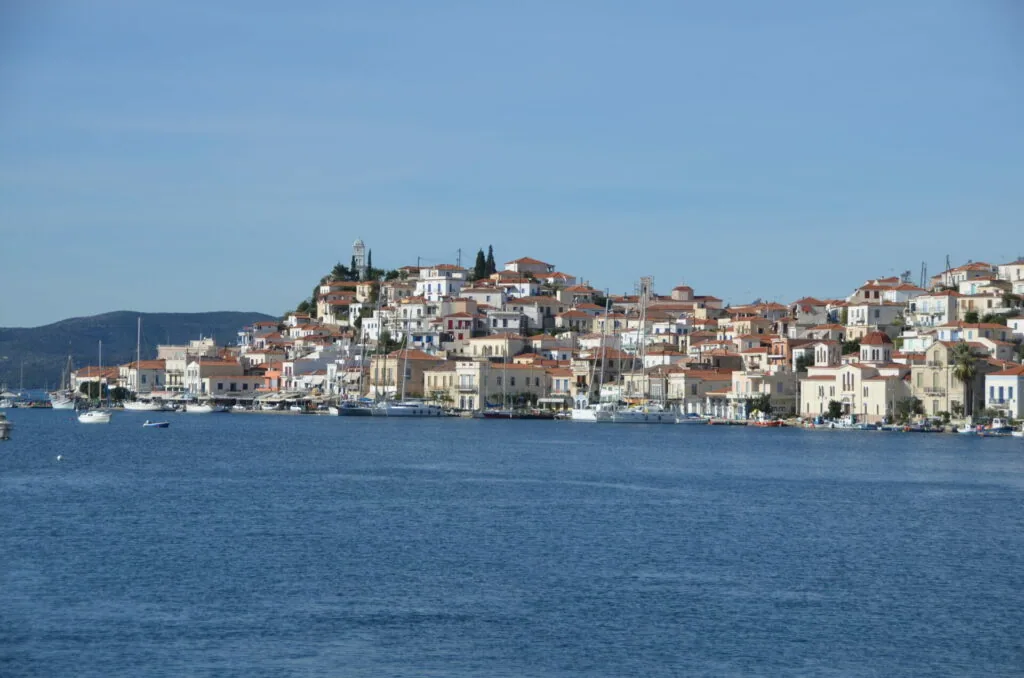 Waterfront hillside town with multi-story buildings in white and terracotta tones overlooking blue water with anchored boats