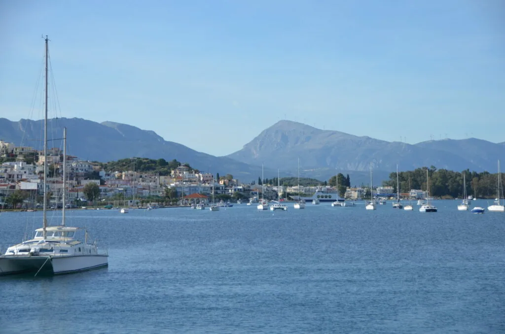 Sailboats anchored in blue water with Mediterranean hillside town and mountains in background