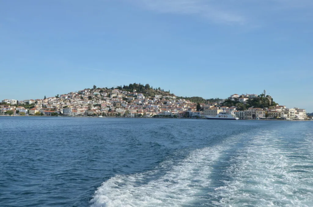 Hillside coastal town with densely packed white buildings overlooking blue water viewed from a boat