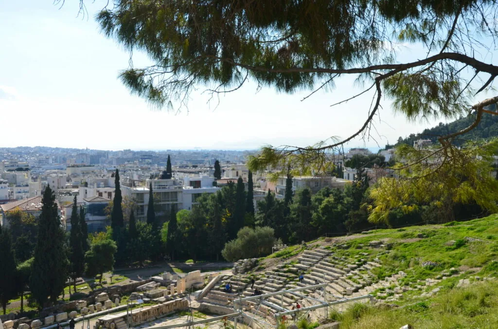 Ancient amphitheater with stone seating overlooking a hillside city with cypress trees and Mediterranean architecture