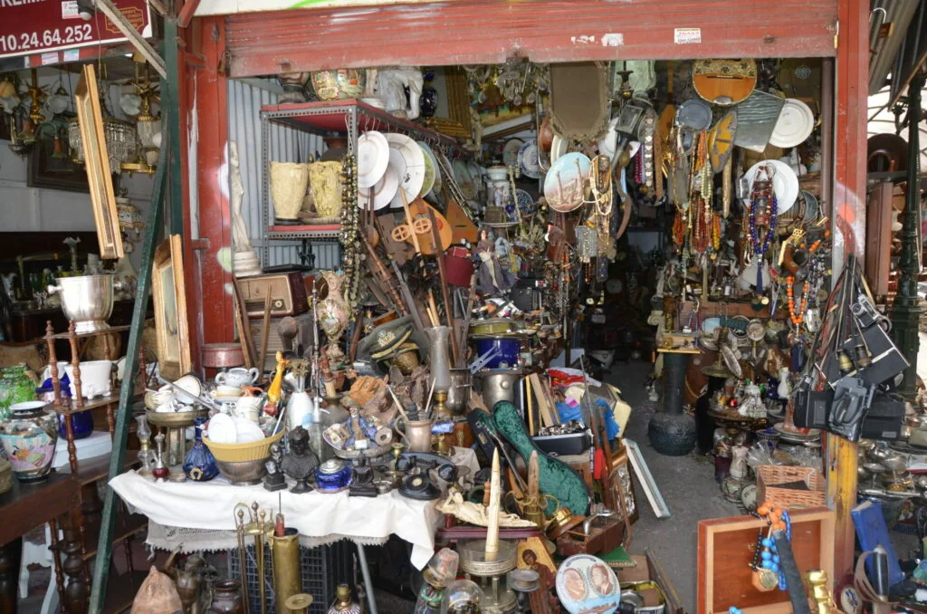 Cluttered antique and vintage shop storefront filled with hanging plates, tools, decorative items, and collectibles