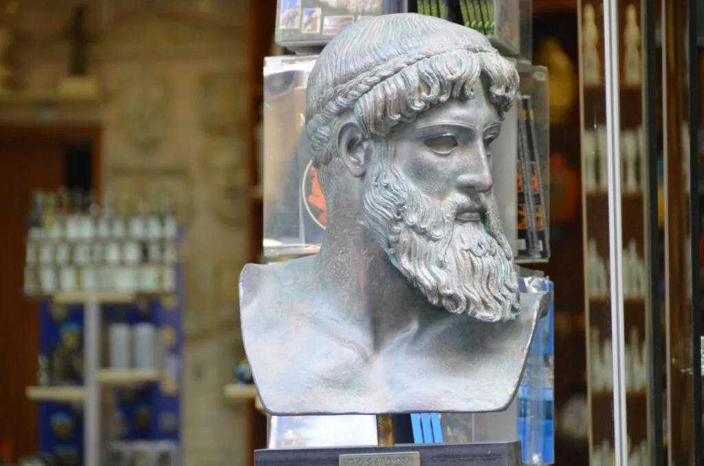 Stone bust sculpture of bearded man with curled hair on display pedestal in museum setting