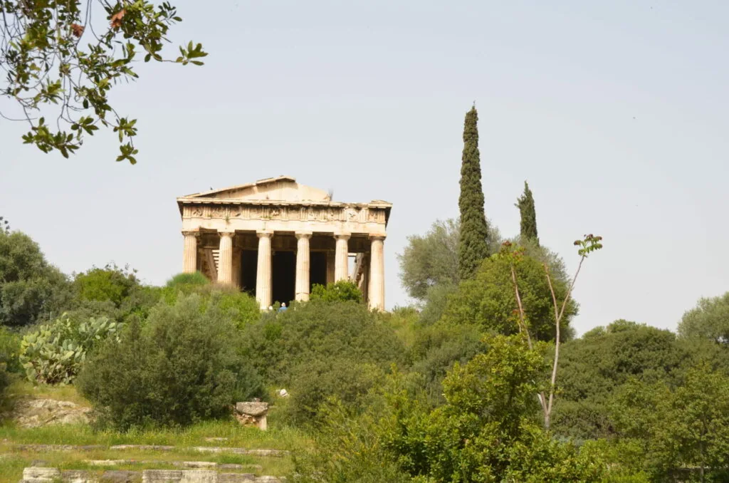 Ancient Greek temple with Doric columns surrounded by olive trees and cypress trees in a natural landscape