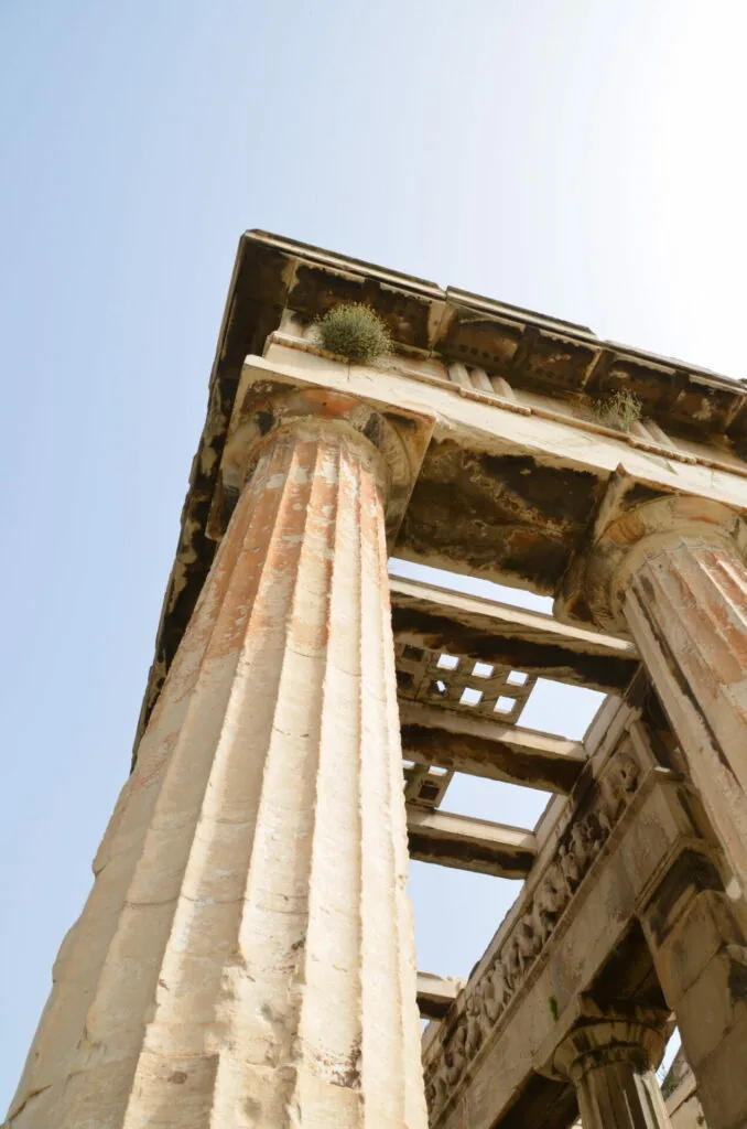 Ancient stone columns with fluted details and weathered capitals, viewed from below against clear blue sky