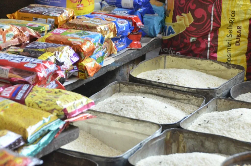 Metal bins filled with white rice and packaged food items displayed at outdoor market stall