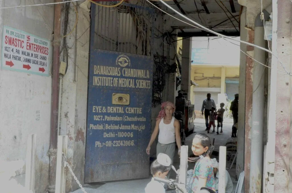 Man and children standing outside an eye and dental medical center entrance in Delhi, with signage visible on weathered building walls
