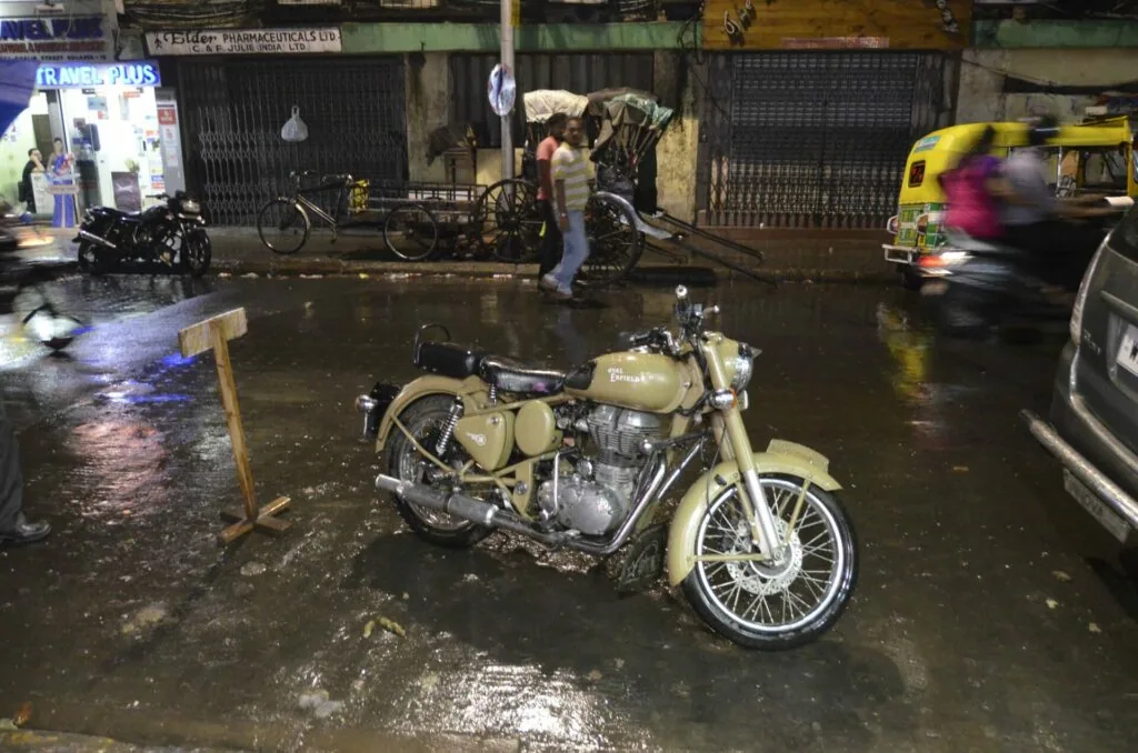 Cream-colored motorcycle parked on wet street at night with shops and vehicles in background