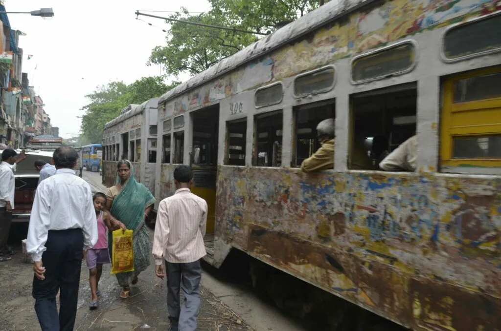 Weathered commuter train with passengers boarding at a platform in an urban area