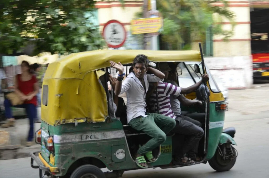 Two men riding in a yellow and green auto-rickshaw on a city street