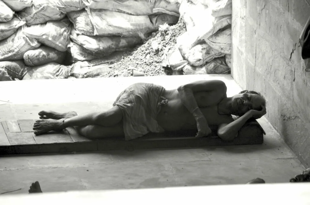 Person lying on concrete floor against wall with stacked bags above