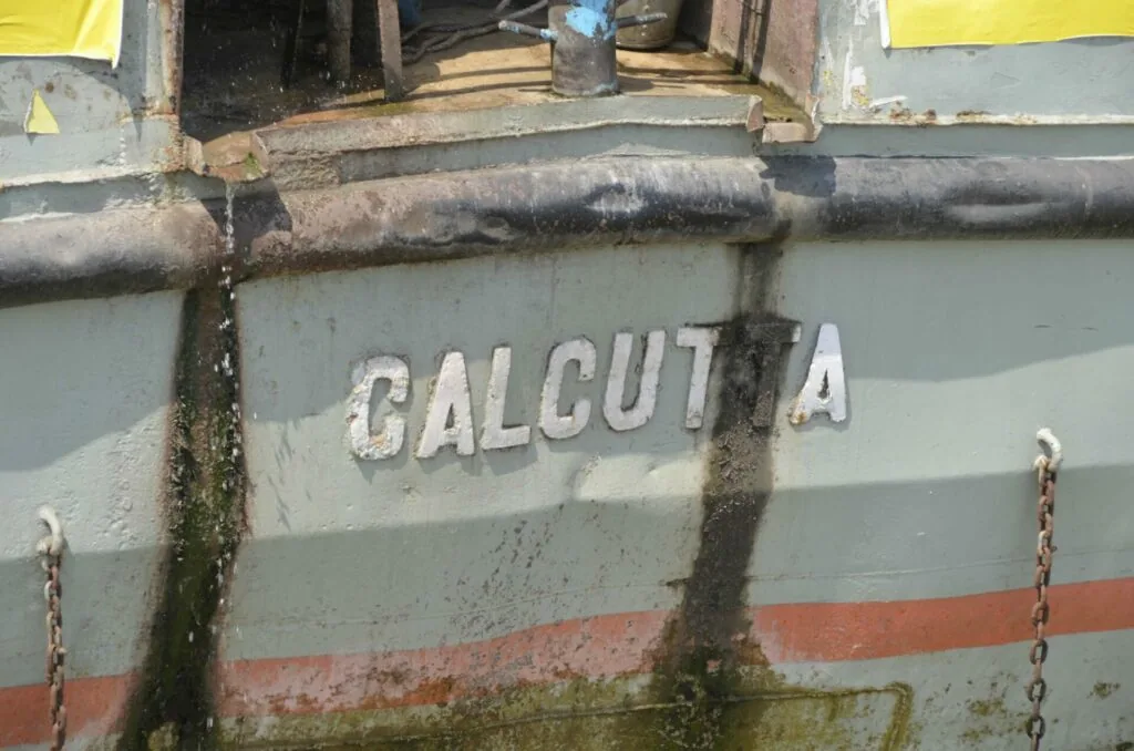 Weathered vessel hull displaying faded white letters spelling CALCUTTA with rust and algae buildup
