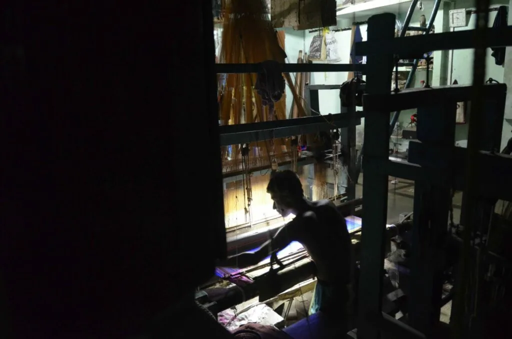Person silhouetted working at illuminated display case in dark interior space with shelving visible in background