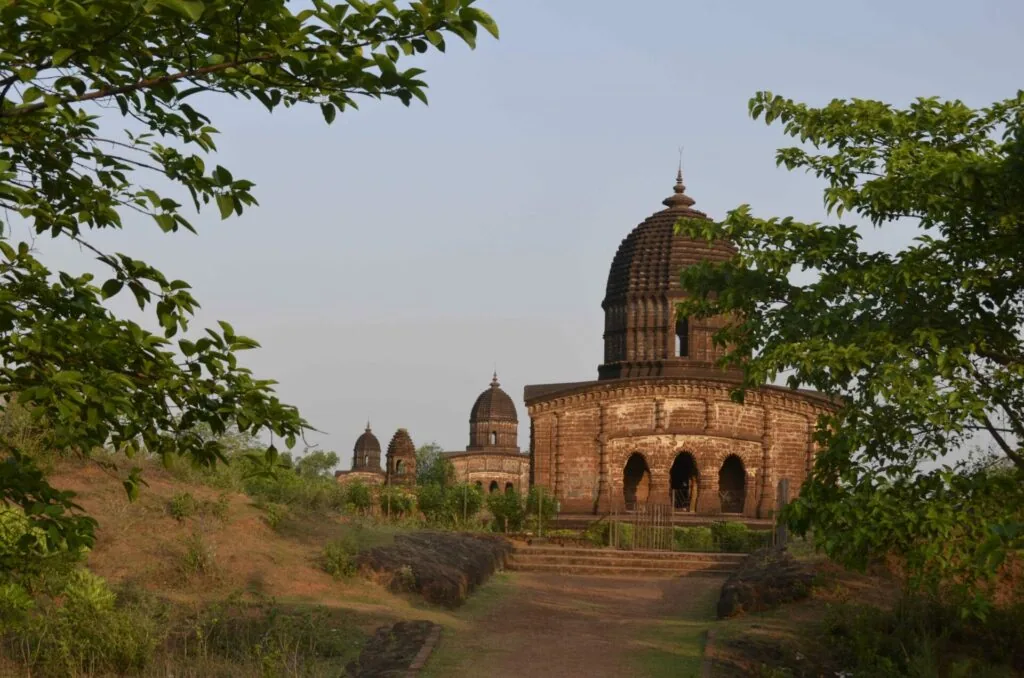 Ancient brick temple with domed architecture surrounded by green trees and vegetation on hillside