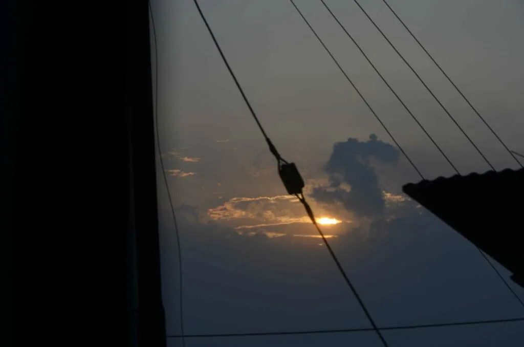 Sailboat rigging silhouetted against dramatic sunset sky with golden light breaking through clouds