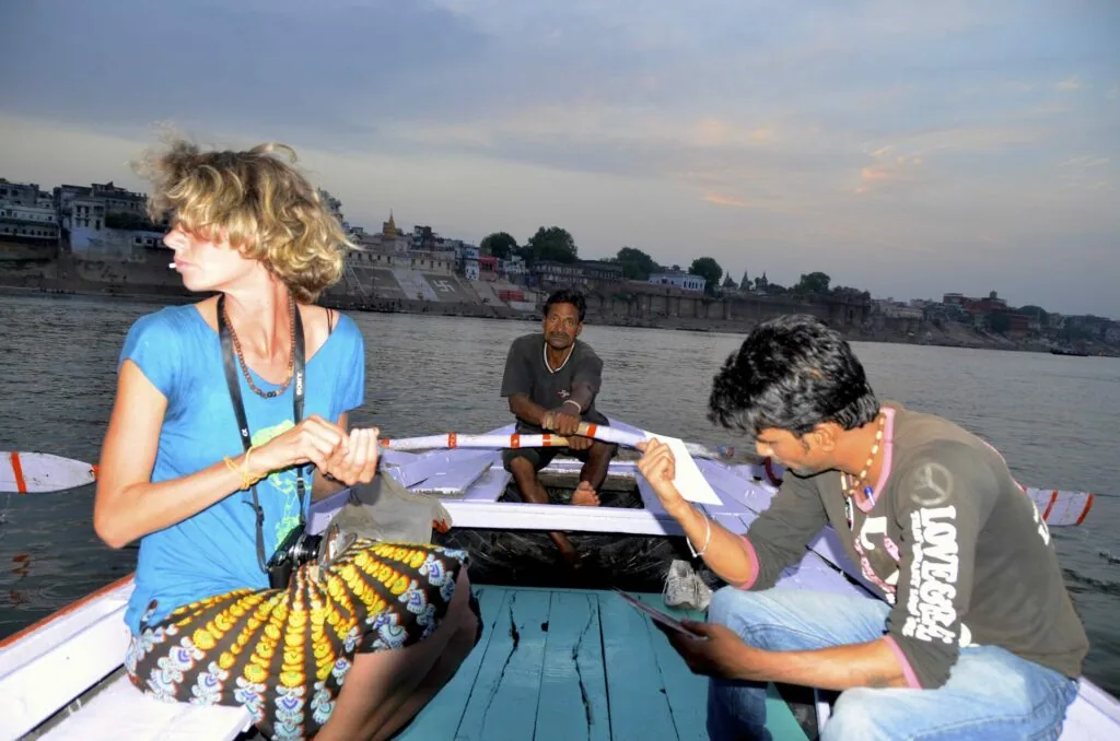 Three people in a rowboat on a river with historic waterfront buildings visible in background