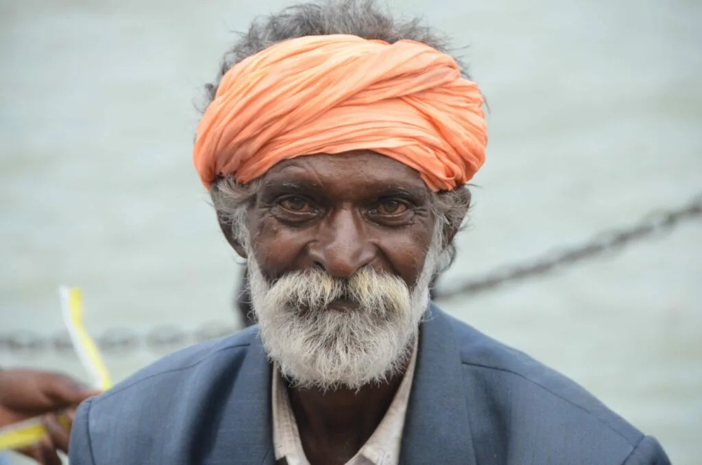 Elderly man with gray beard wearing orange turban and dark blue shirt