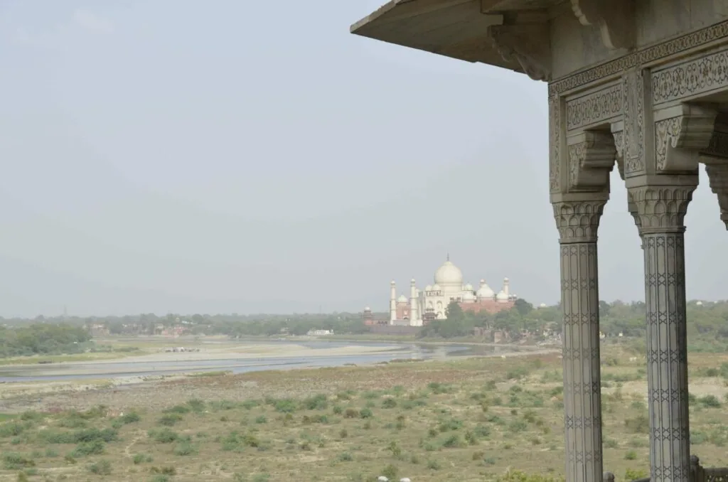 Ornate marble pavilion with carved columns overlooking a river and distant domed monument across landscaped grounds