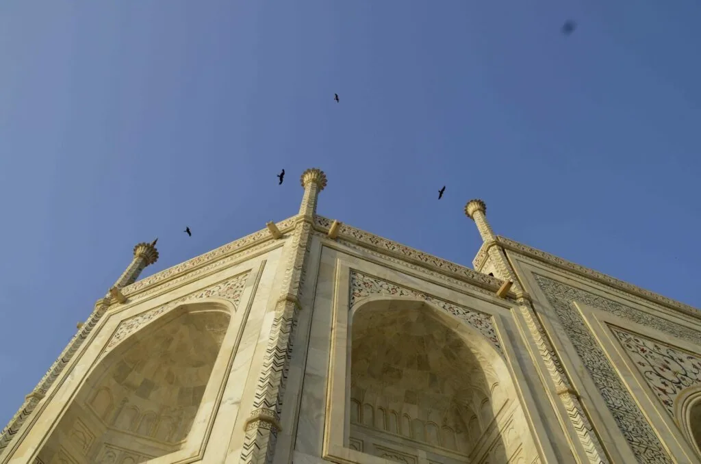 Ornate white marble building with decorative finials against clear blue sky and birds flying