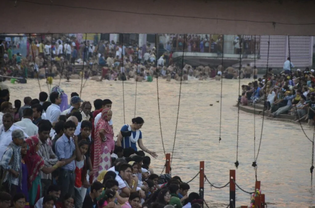Crowds of people gathered at the edge of water with ropes and wooden posts, spectators standing on both sides