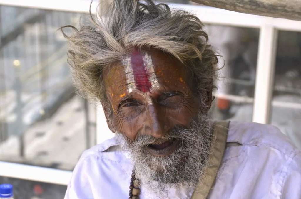 Elderly man with gray hair and beard wearing white shirt and religious markings on forehead