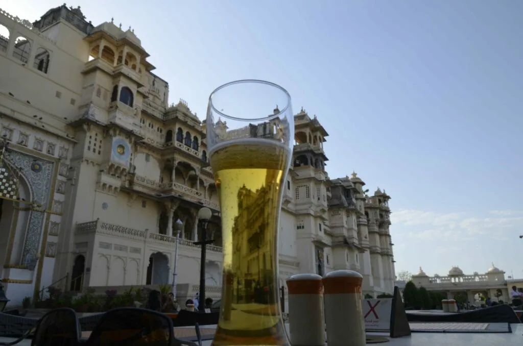 Glass of yellow beer in front of ornate Indian palace architecture with multiple levels and domed turrets