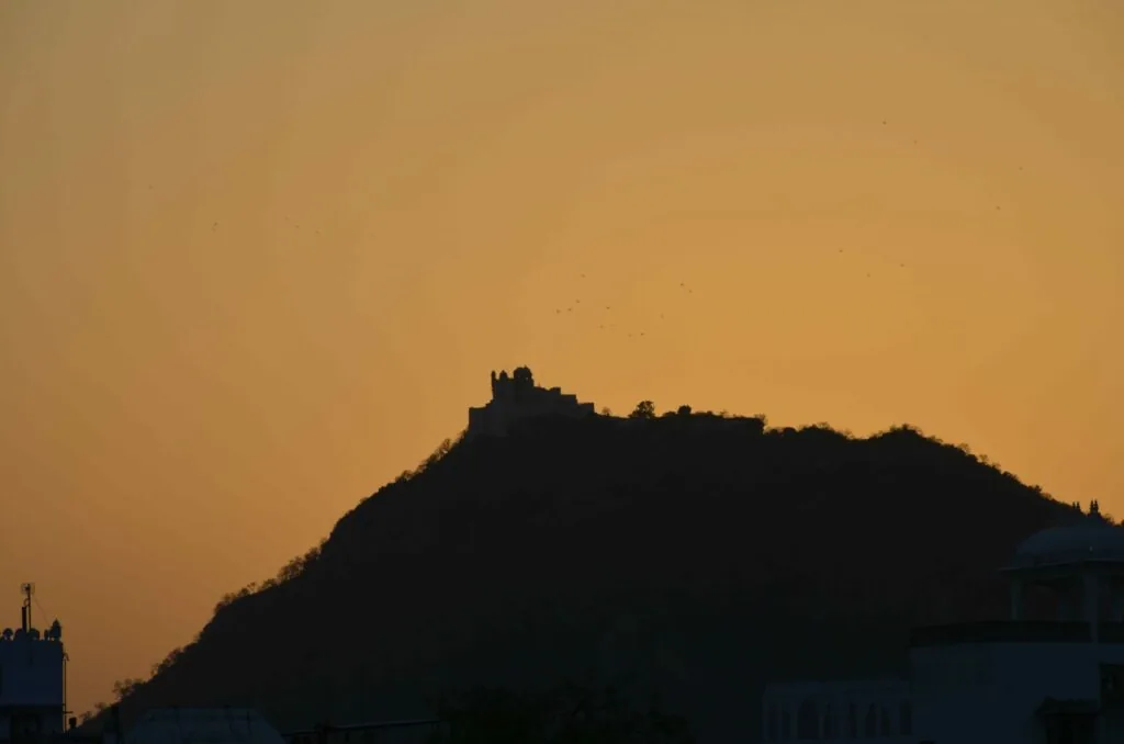 Silhouette of a hilltop with ruins and structures against an orange sunset sky