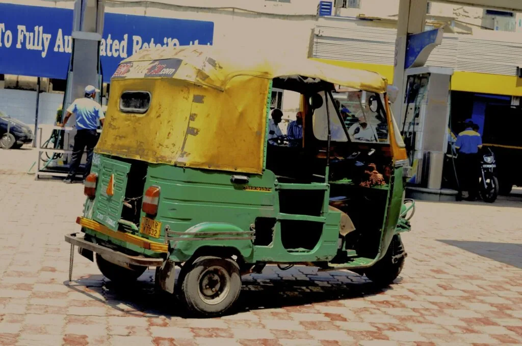 Green and yellow auto rickshaw parked on brick pavement with buildings and people in background