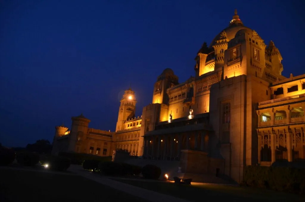 Illuminated palace with ornate architecture and multiple domes against dark blue evening sky