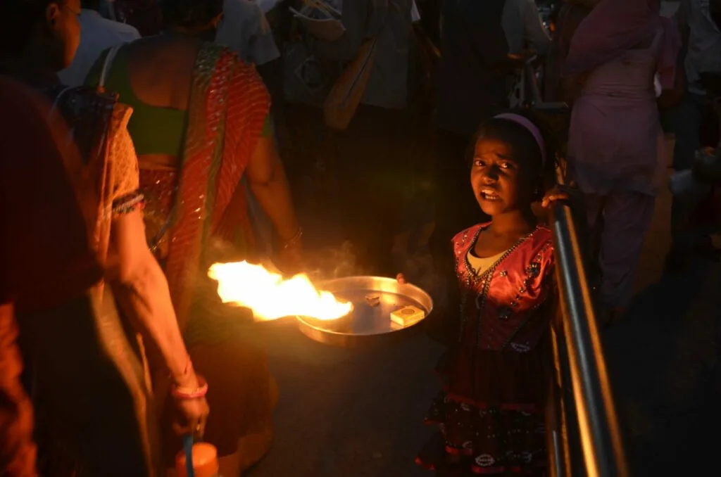 Child watching person hold flaming torch at night gathering