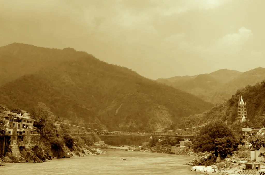 Sepia-toned landscape of a river valley with a suspension bridge, pagoda tower, and forested mountains