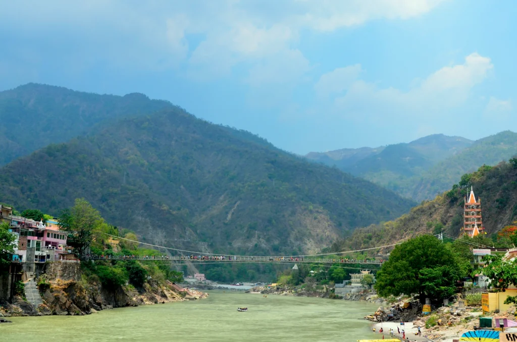River valley with green mountains, suspension bridge, and orange temple tower in mountainous landscape